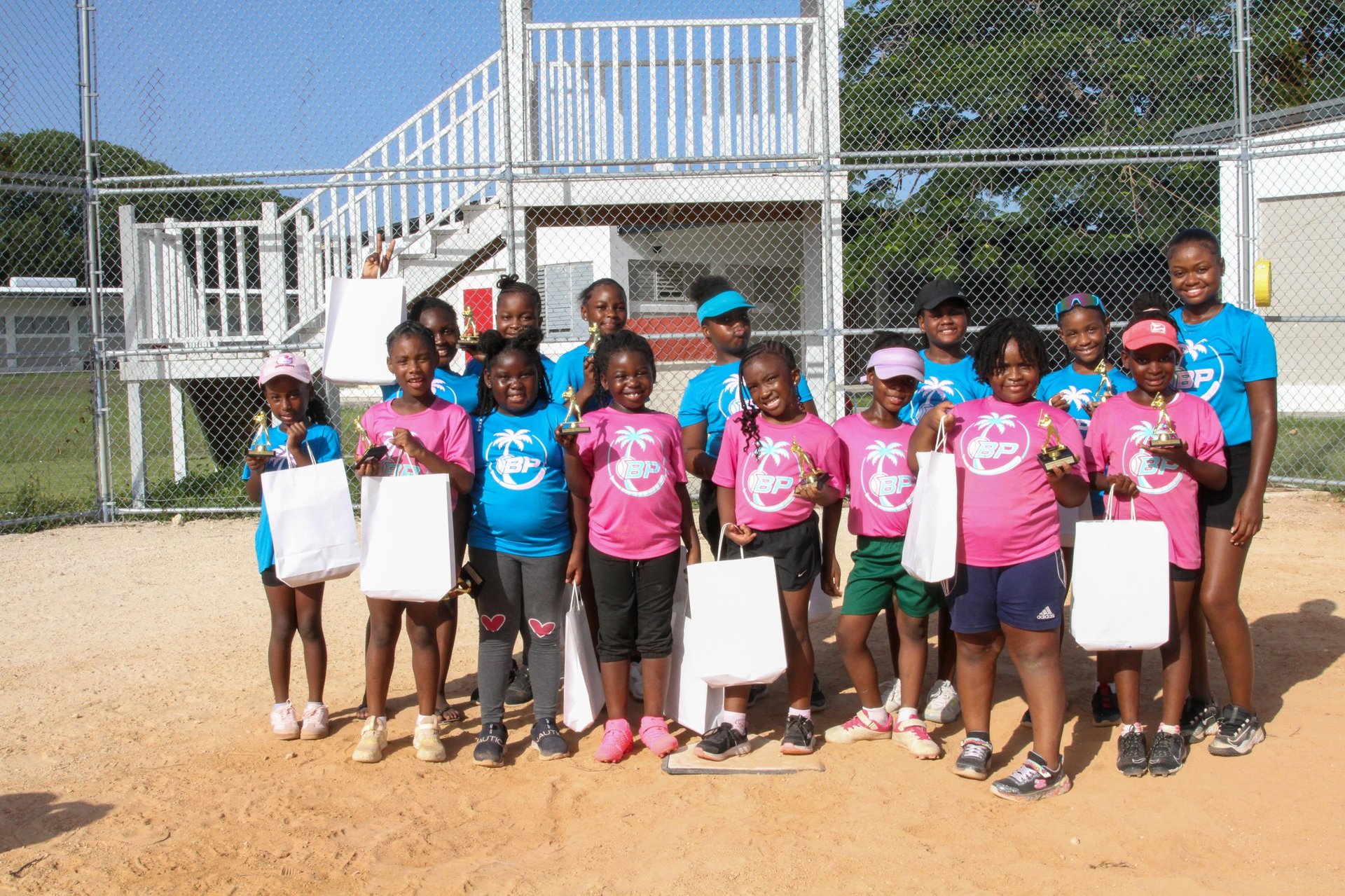 Group of children wearing pink and blue shirts holding blank signs at a baseball field with dugout in background
